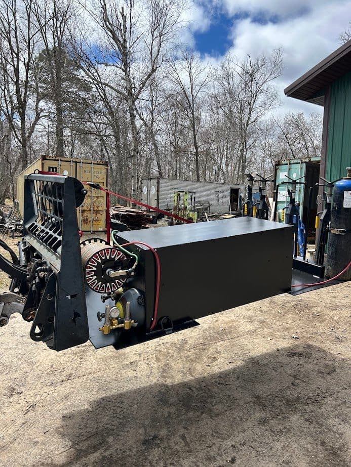 Heavy-duty machinery with a black box and wheel, set against a wooded background.