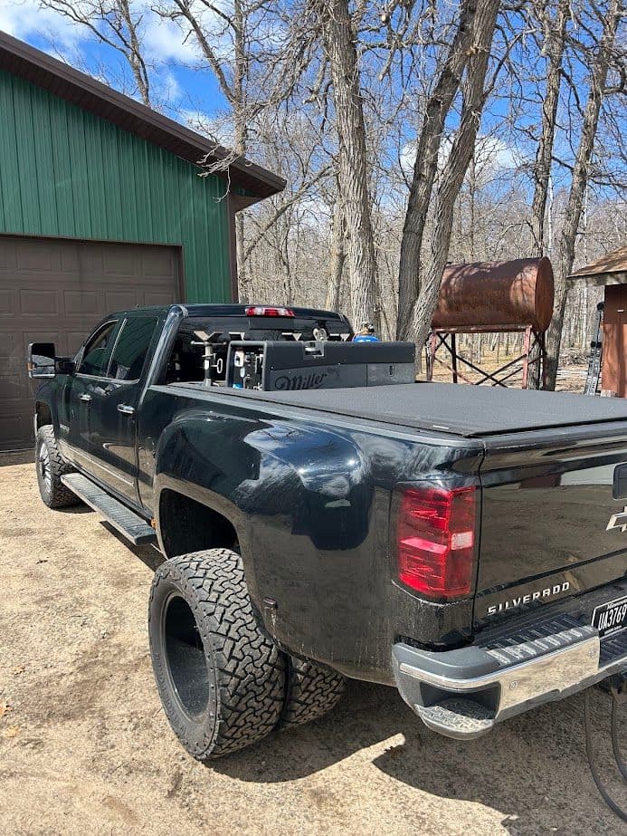 Black Chevrolet Silverado truck with custom wheels parked near trees and a garage.