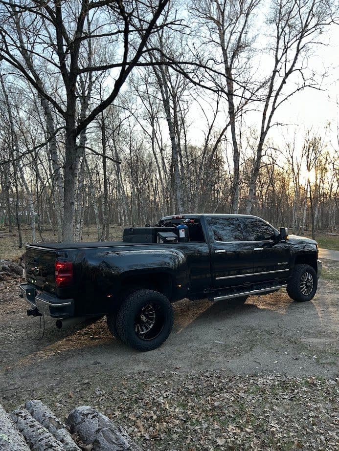 Black pickup truck parked in a wooded area at sunset, showcasing rugged off-road tires.