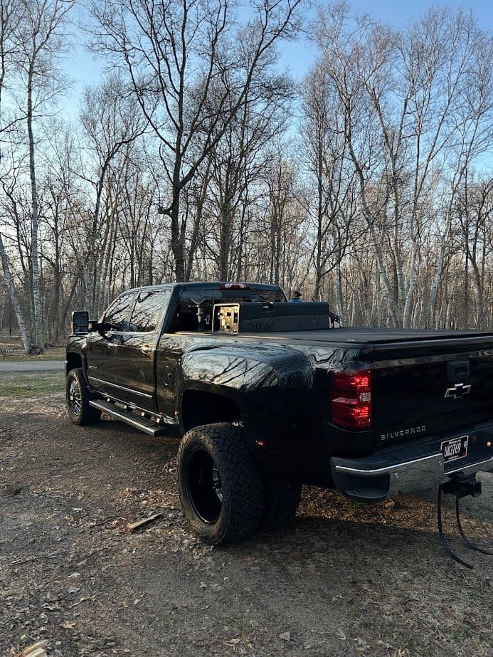 Black Chevrolet Silverado truck parked in a wooded area with trees in the background.