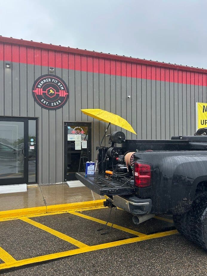 Exterior of Hammer Fit gym with a yellow umbrella by a pickup truck on a rainy day.