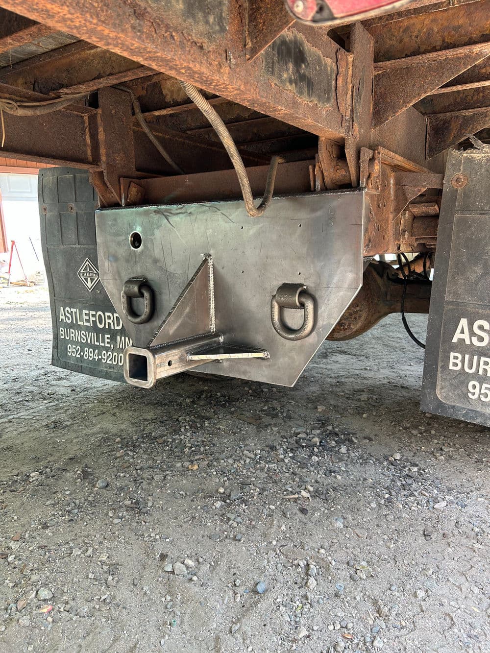 Metal hitch assembly under a truck, featuring safety hooks and a sturdy design for towing.