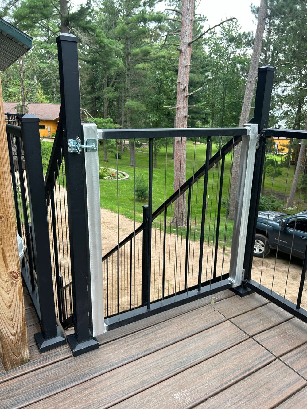 Black metal gate on a wooden deck with a forest background, ideal for safety and access.