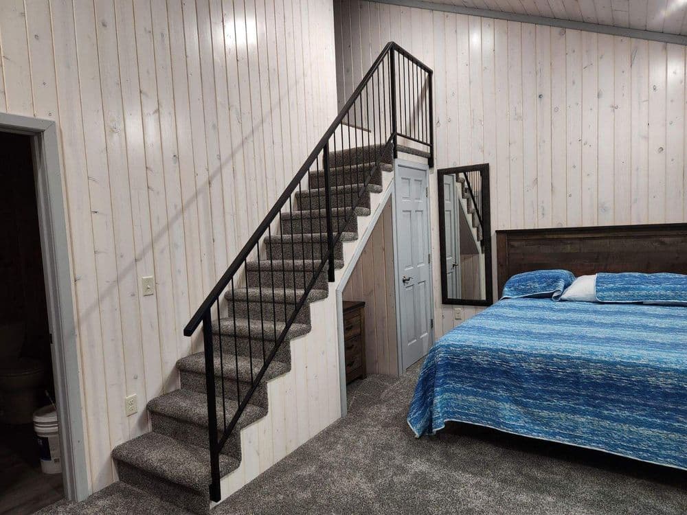 Cozy bedroom with blue bedding, stairs, and wooden accent wall in modern design.