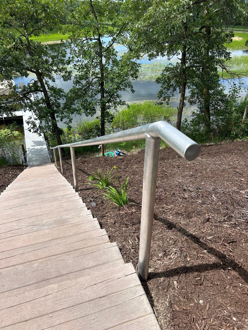 Handrail on wooden steps leading down to a serene lake surrounded by greenery.