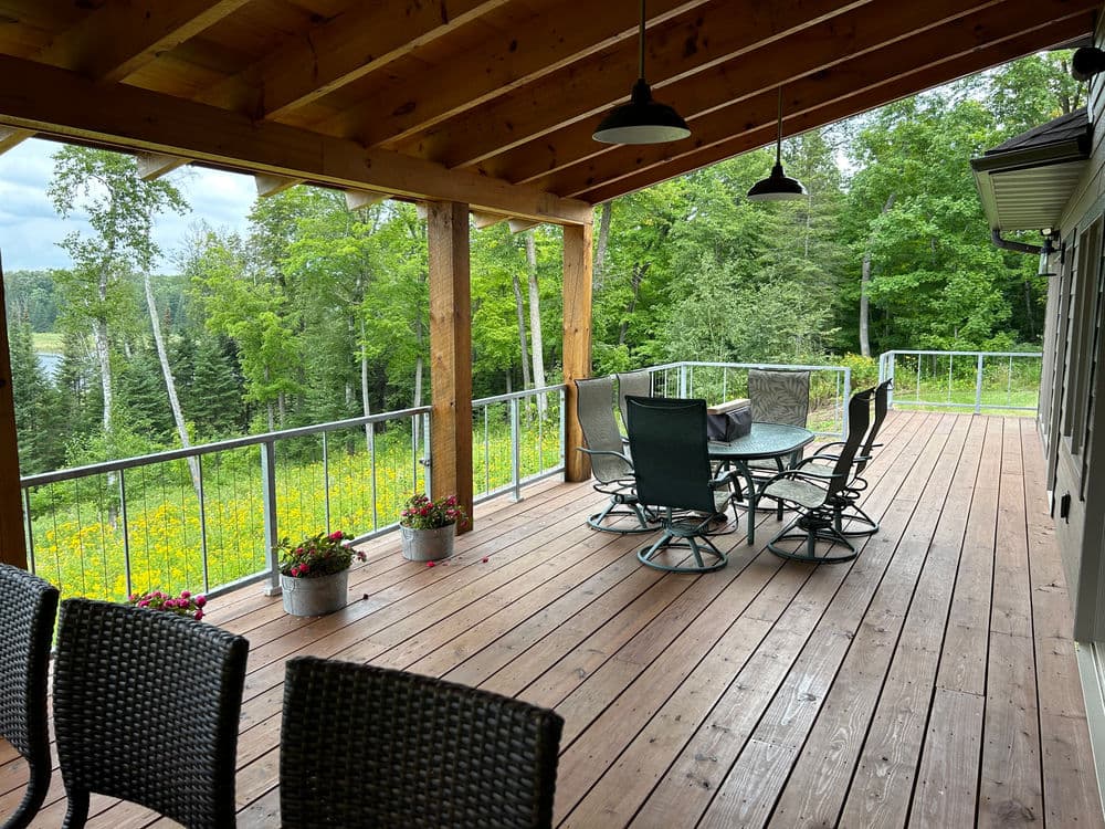 Spacious wooden outdoor deck with dining set and scenic views of lush greenery.