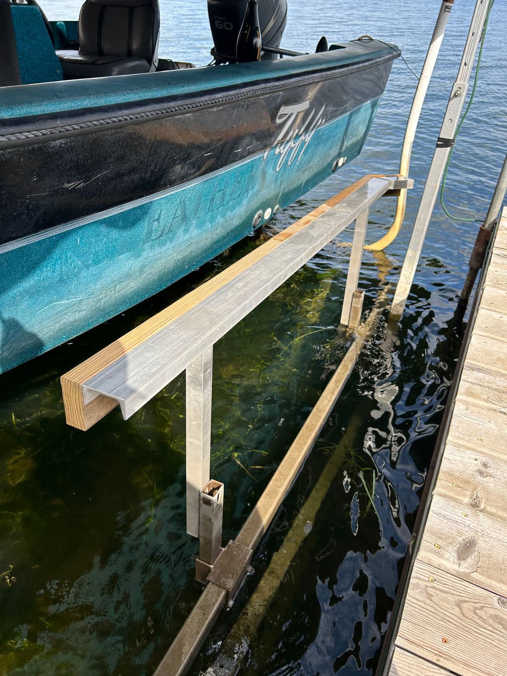 Boat lift with aluminum frame alongside a dock in calm water, featuring aquatic plants below.