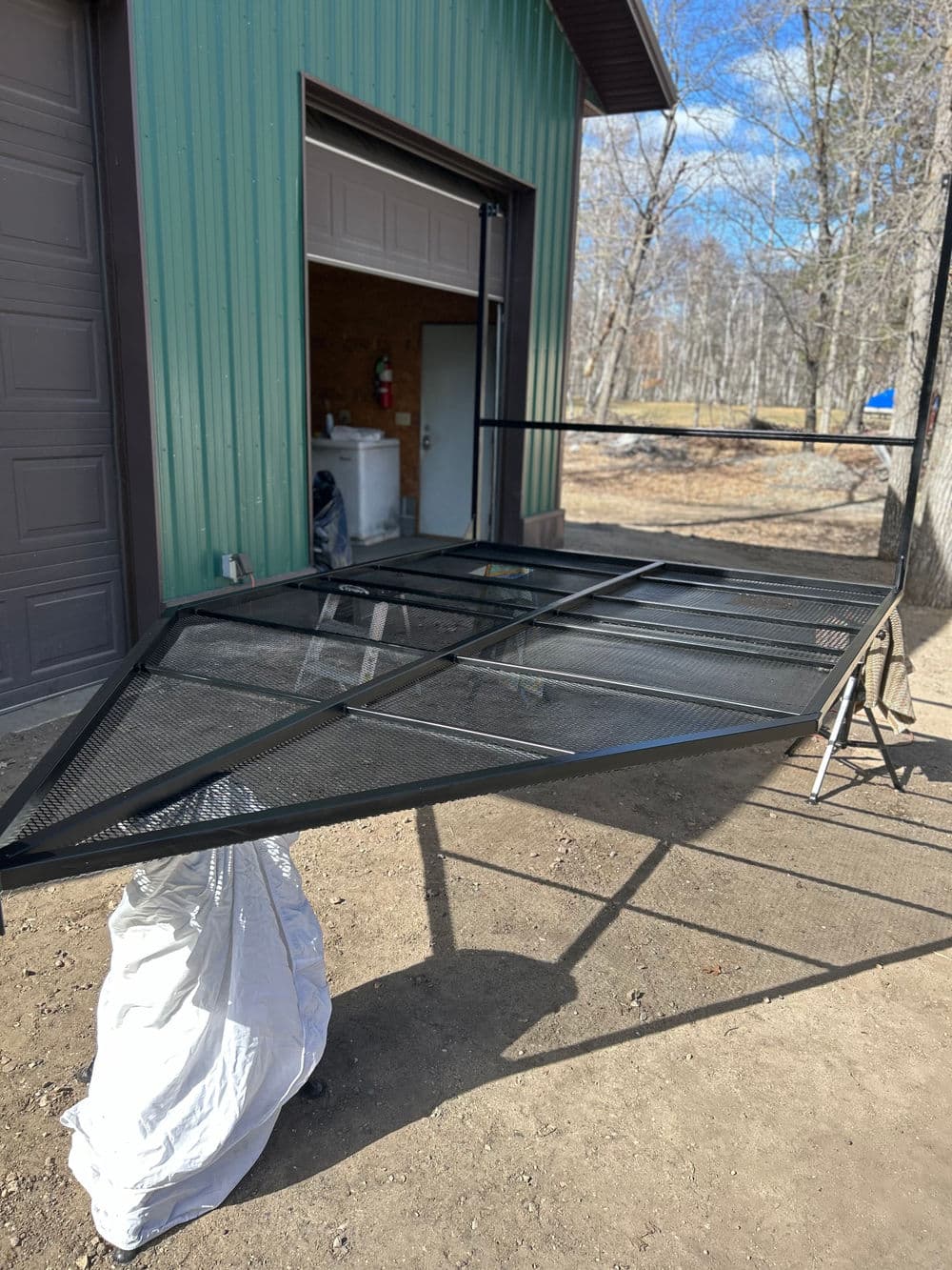 Metal outdoor cart frame in workshop, showing black mesh design and open garage door background.