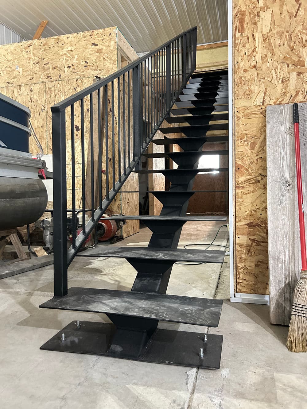Metal industrial staircase with black railing and open risers in a workshop setting.