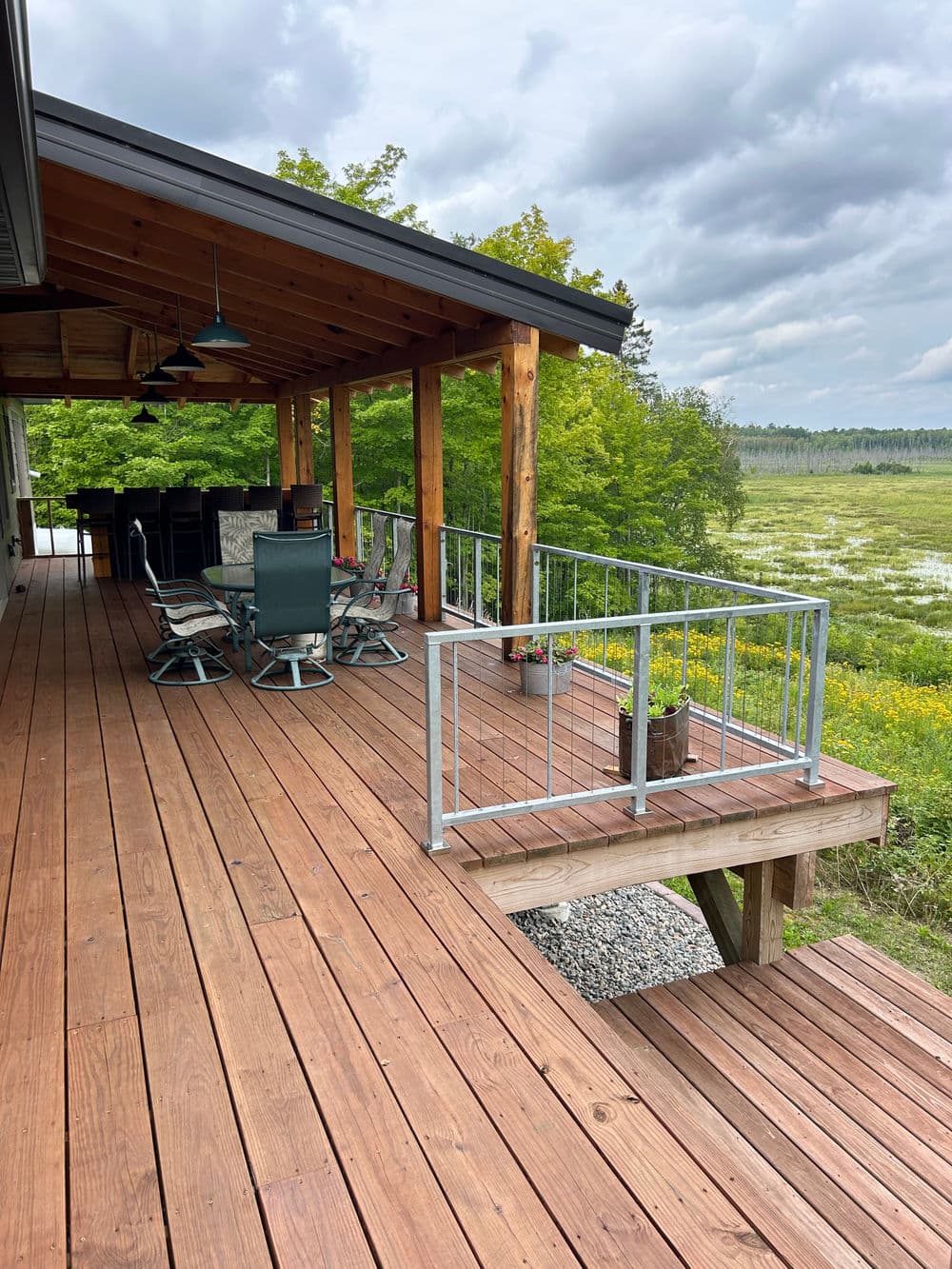 Spacious wooden deck with railing, outdoor seating, and scenic view of green landscape.