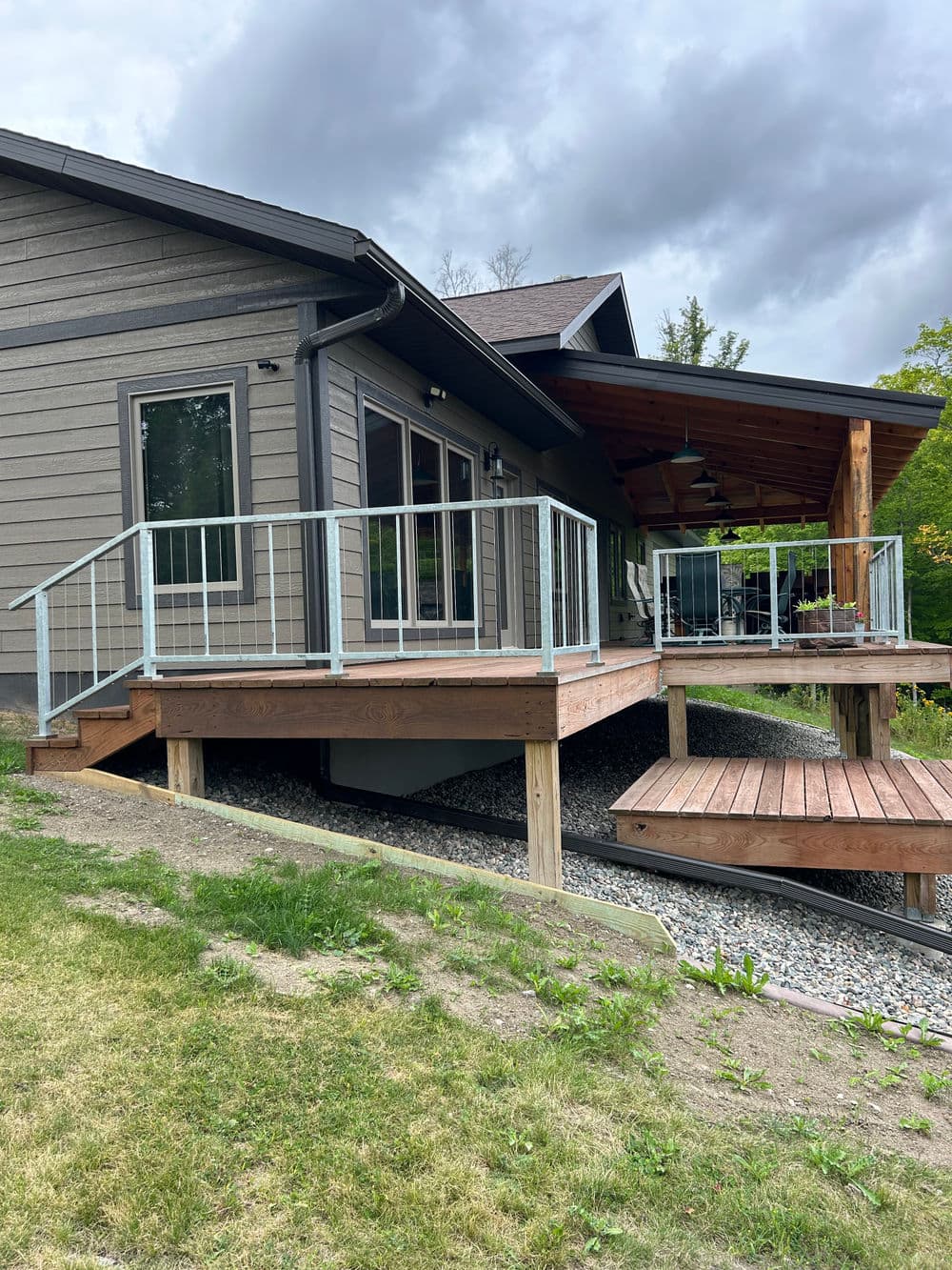 Modern home exterior with wooden deck and railings, surrounded by greenery under a cloudy sky.