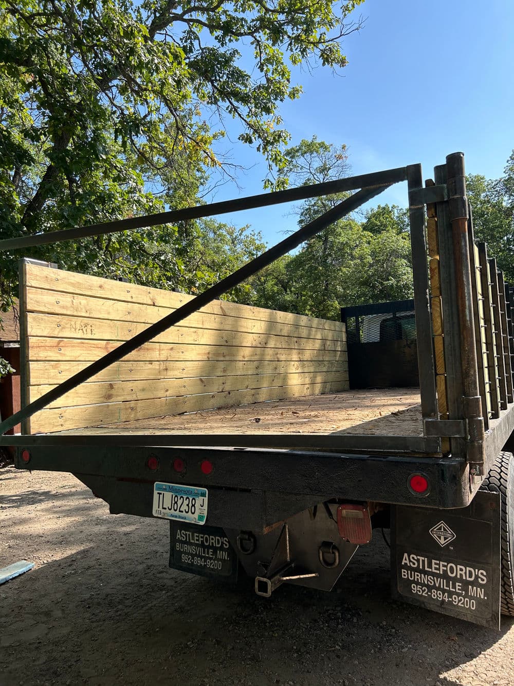 Flatbed truck with wooden side rails parked in a wooded area, Astleford's Burnsville, MN.